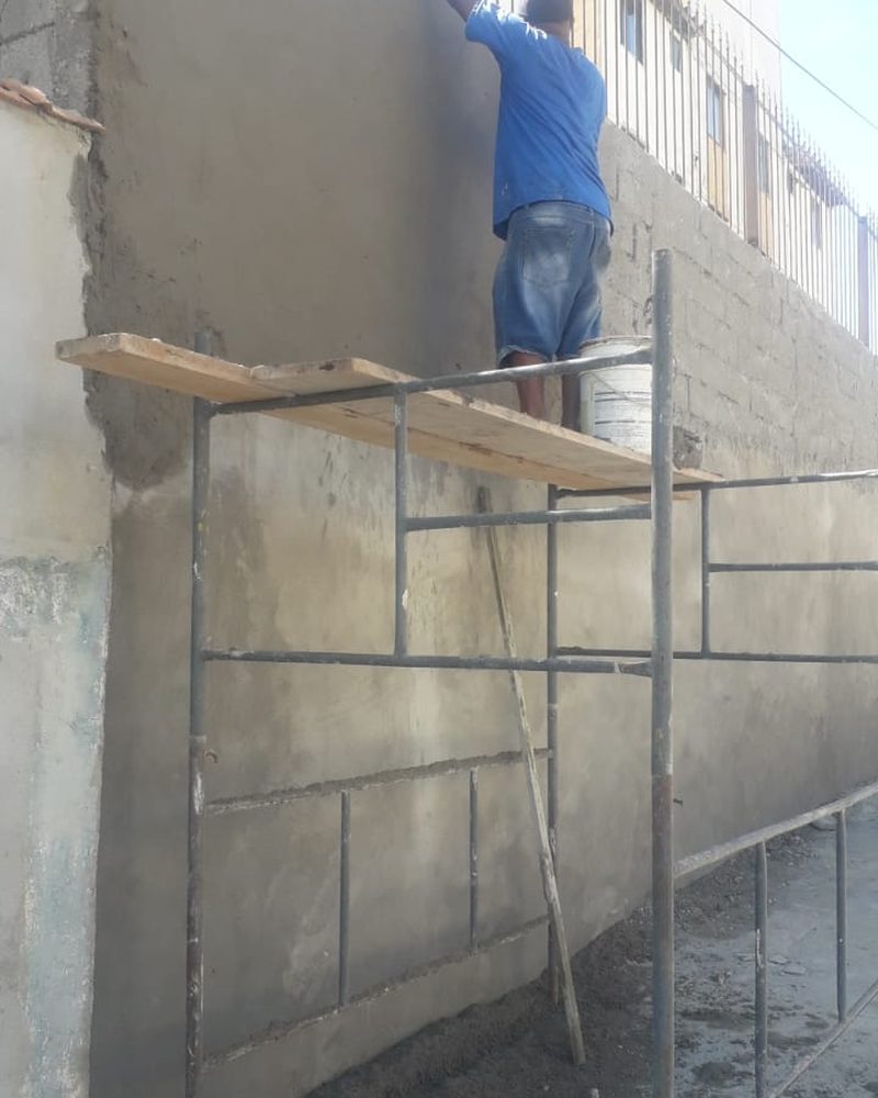 Pedreiro aplicando reboco em muro externo sobre andaime