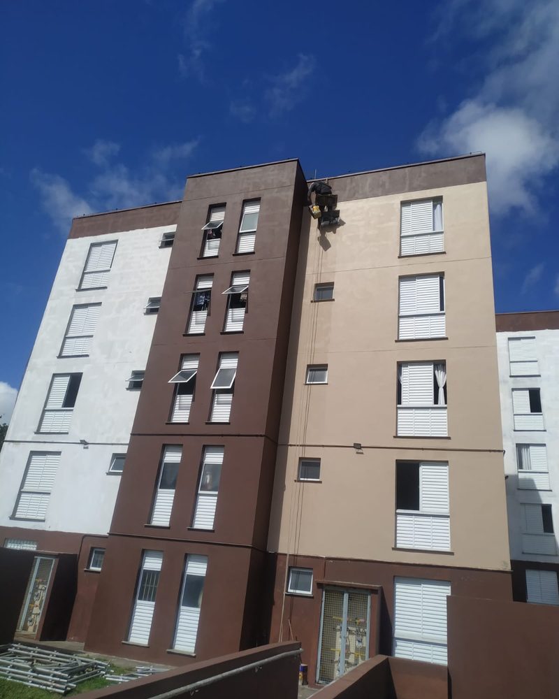 Pintor em balancim aplicando tinta na fachada de um edifício residencial