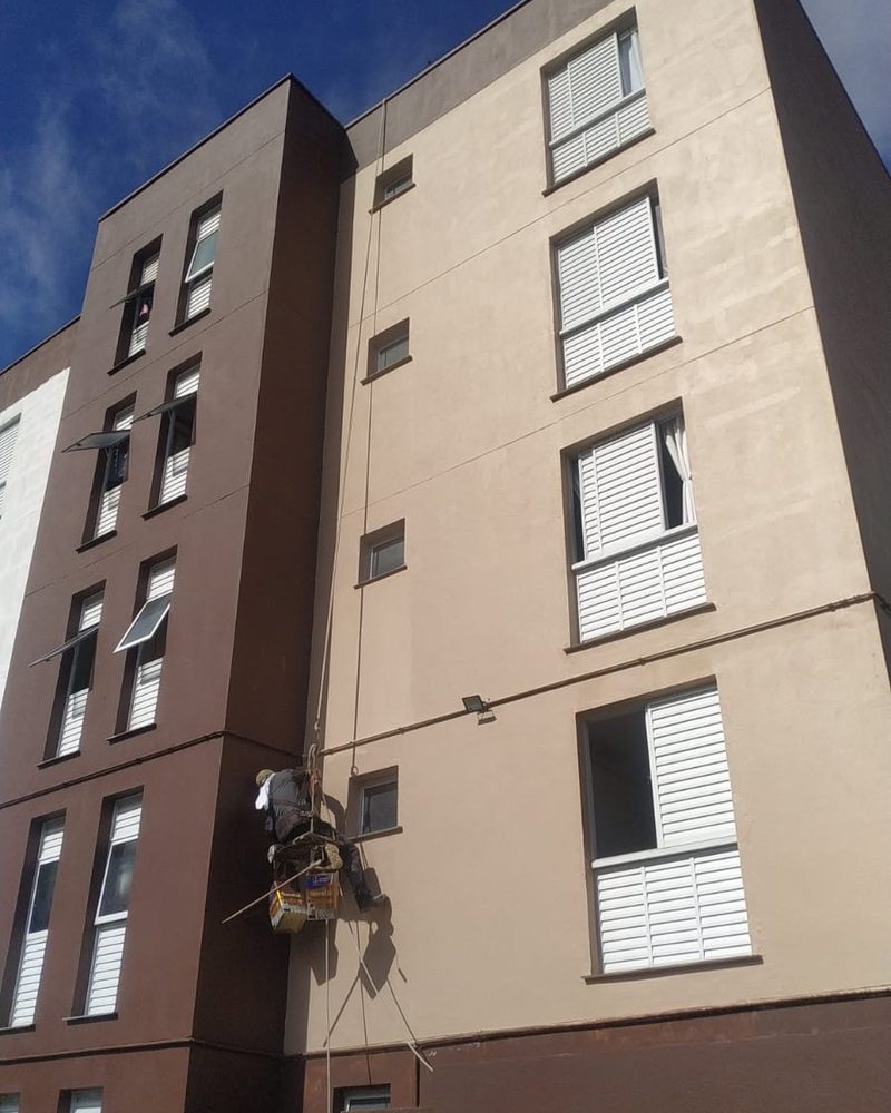 Pintor suspenso concluindo a pintura da fachada de um bloco residencial
